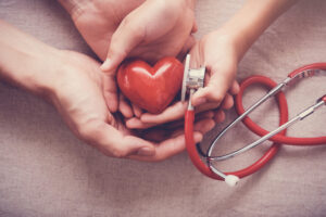 child and adult holding red heart with stethoscope, heart health