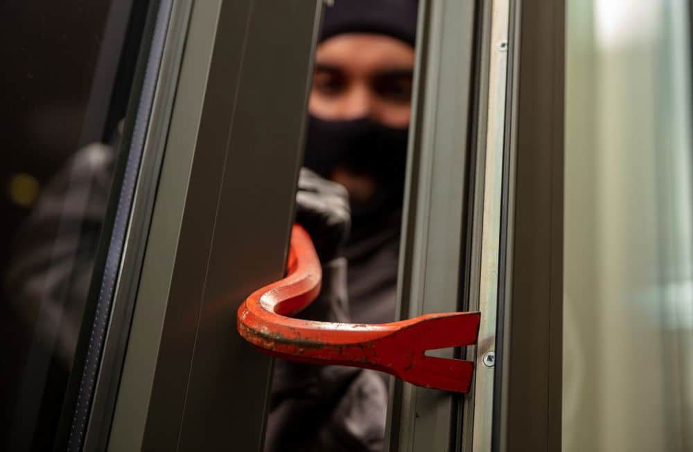 thief in balaclava holding a crowbar to break a glass