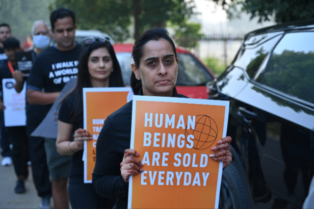 A medium-close shot features a group of people walking along a street, apparently participating in a protest or march.